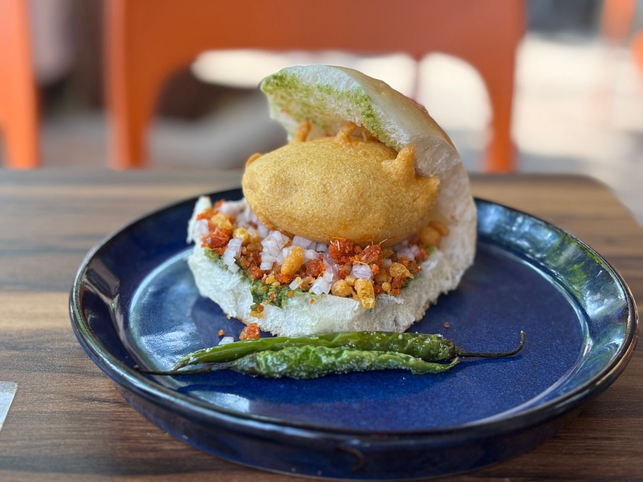 Close-up of a traditional Indian vada pav served with a green chili on a ceramic plate.